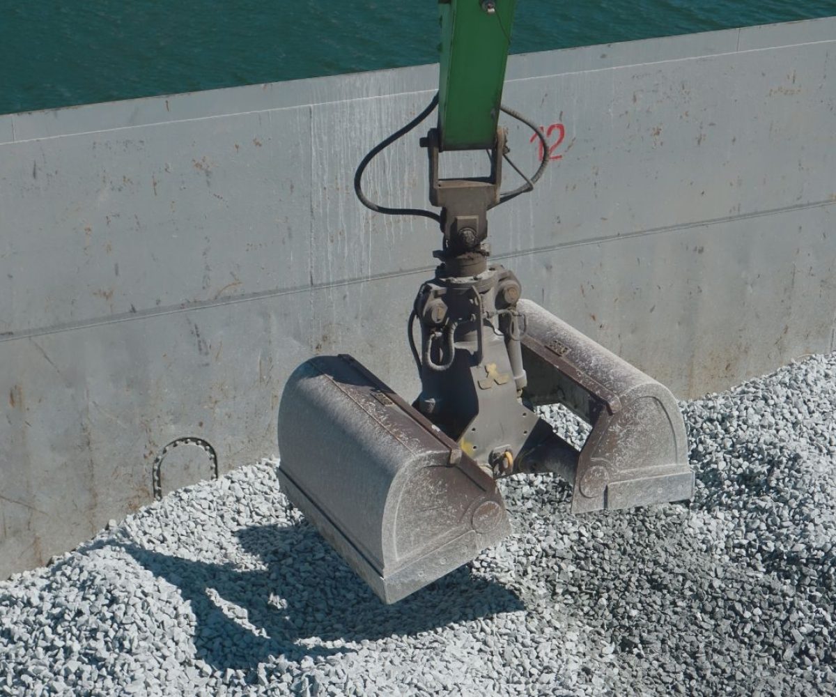 Greifer entlädt Gleisschotter aus einem Binnenschiff im Baustoffzentrum Ruhrtal am Dortmunder Hafen.